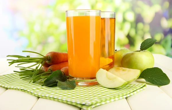 Glazen van SAP, appelen en wortelen op witte houten tafel, op groene achtergrond — Stockfoto
