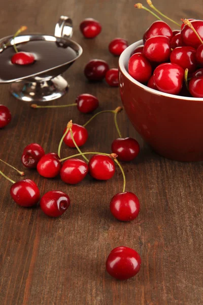 Reife rote Kirschbeeren in Tasse und Schokoladensauce auf Holztisch in Großaufnahme — Stockfoto