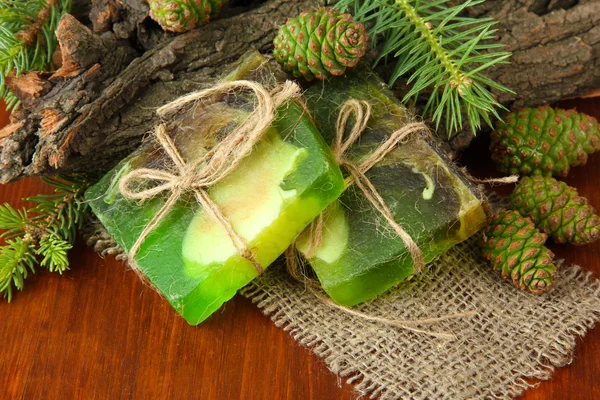 Handgemaakte zeep en groene dennenappels op houten tafel — Stockfoto