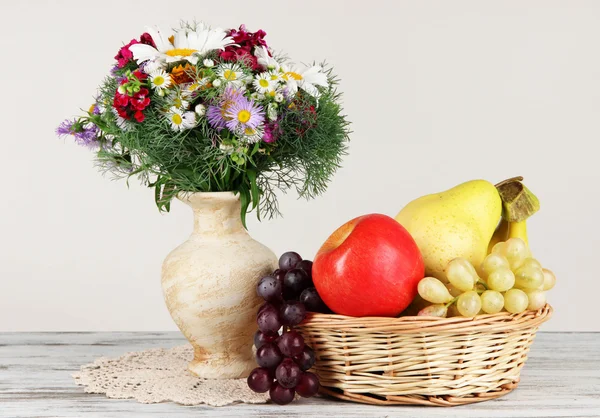 Mooie heldere bloemen in vaas met fruit op tafel op grijze achtergrond — Stockfoto