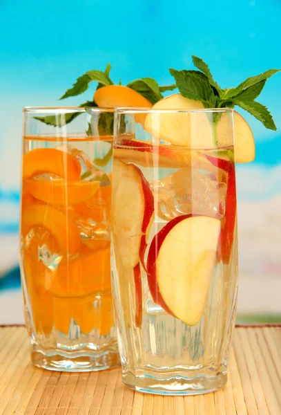 Glasses of fruit drinks with ice cubes on blue background — Stock Photo, Image