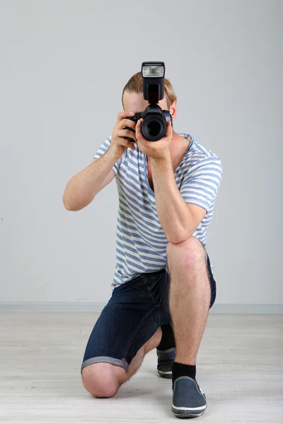 Schöner Fotograf mit Kamera, auf grauem Hintergrund — Stockfoto