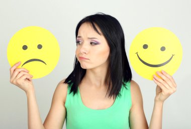 mutlu ve üzgün smiley ile kağıt gri arka plan üzerinde tutan genç kadın