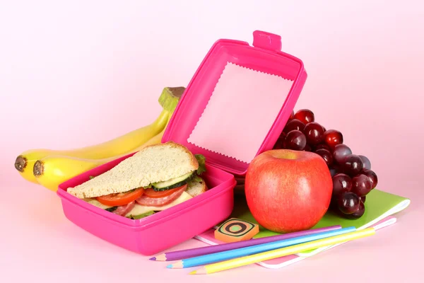 Matlåda med smörgås, frukt och pappersvaror på rosa bakgrund — Stockfoto