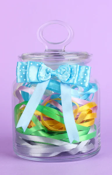 Vaso di vetro contenente vari nastri colorati su sfondo lilla — Foto Stock