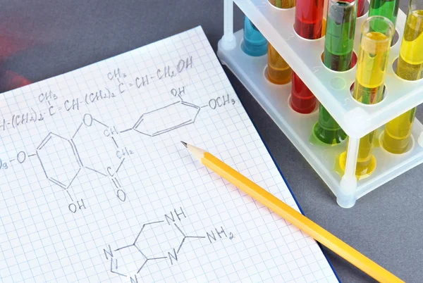 Tubos de ensaio com líquidos e fórmulas coloridas sobre fundo cinzento — Fotografia de Stock
