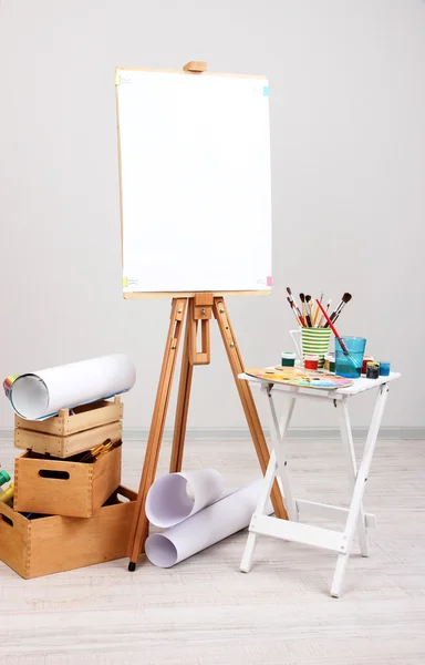 Wooden easel with clean paper and art supplies in room — Stock Photo, Image