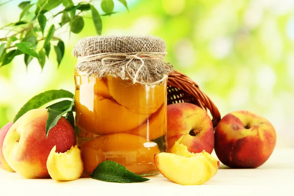 Jar of canned peaches and fresh peaches on wooden table, outside