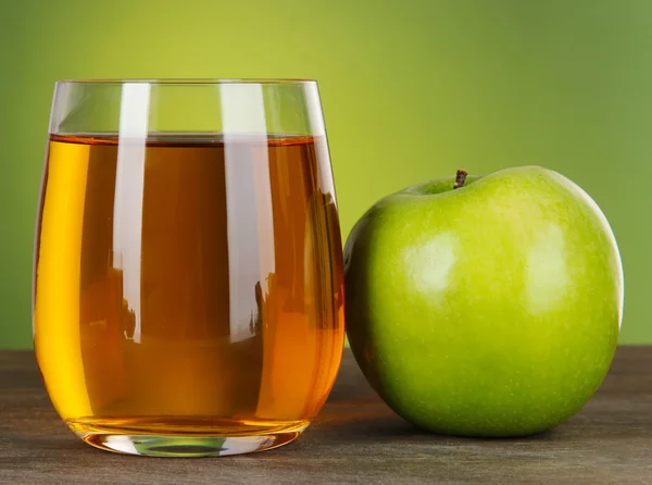 Glass of fresh apple juice on table on green background — Stock Photo, Image