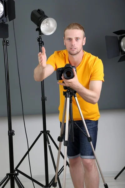 Bello fotografo con macchina fotografica al lavoro, su sfondo studio fotografico — Foto Stock