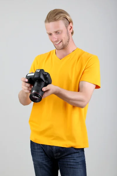 Schöner Fotograf mit Kamera, auf grauem Hintergrund — Stockfoto