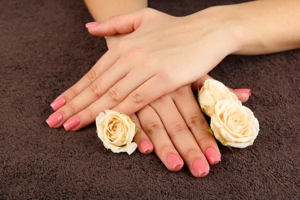 Mãos de mulher com manicure rosa e flores, em fundo de cor — Fotografia de Stock