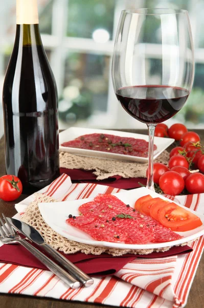 Tasty salami on plates on wooden table on window background — Stock Photo, Image