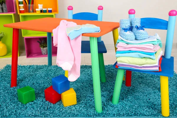 Mesa pequena e colorida e cadeiras com roupas de bebê — Fotografia de Stock