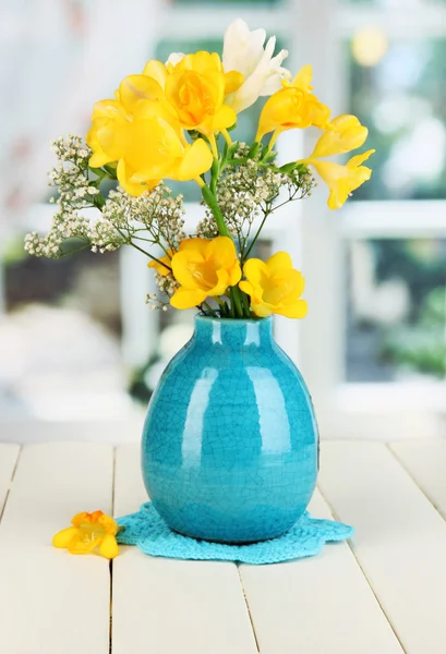 Krásnou kytici freesia v modrou vázu na dřevěný stůl na pozadí okna — Stock fotografie