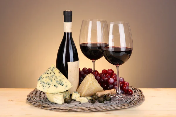 Wyrafinowane martwa wino, sery i winogron na Wiklinowy taca na drewnianym stole na beżowym tle — Zdjęcie stockowe