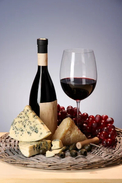 Vida morta refinada de vinho, queijo e uvas em bandeja de vime em mesa de madeira em fundo azul — Fotografia de Stock