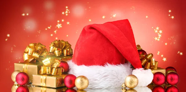 Güzel Noel şapka, hediyeler ve Noel topları sparkles kırmızı zemin üzerine — Stok fotoğraf