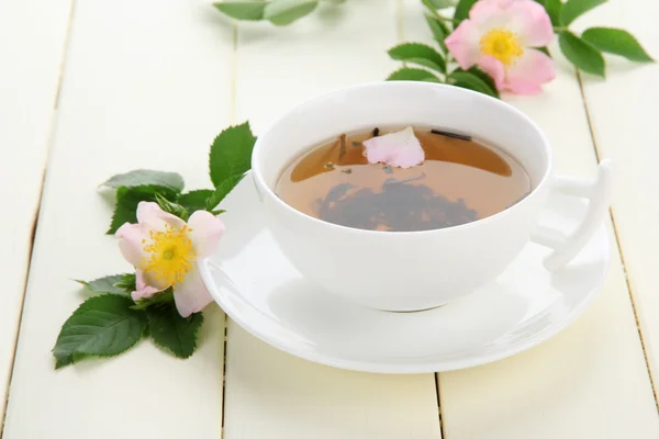 白い木製のテーブルに股関節のバラの花でハーブのお茶のカップ — ストック写真