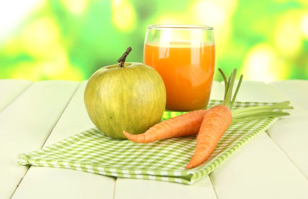 Un mucchio di carote e mela verde, vetro di succo, su tavolo di legno a colori su sfondo brillante — Foto Stock