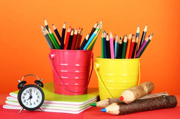 Crayons colorés en deux seaux avec copybooks sur table sur fond orange — Photo