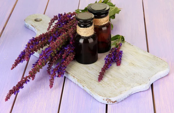 Geneeskundeflessen en salvia bloemen op paarse houten achtergrond — Stockfoto