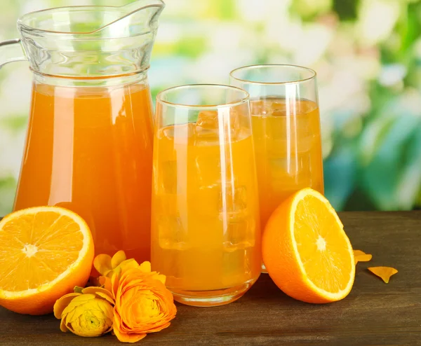 Glasses and pitcher of orange juice on wooden table, on green background — Stock Photo, Image