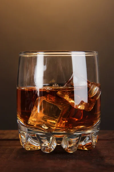 Brandy glass with ice on wooden table on brown background — Stock Photo, Image