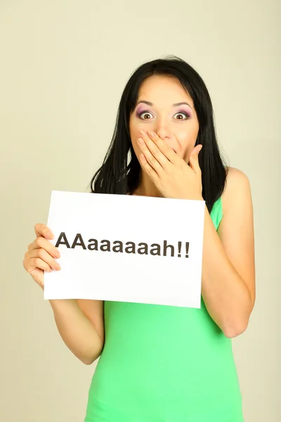 Überraschte junge Frau hält Inschrift "ah" auf grauem Hintergrund — Stockfoto
