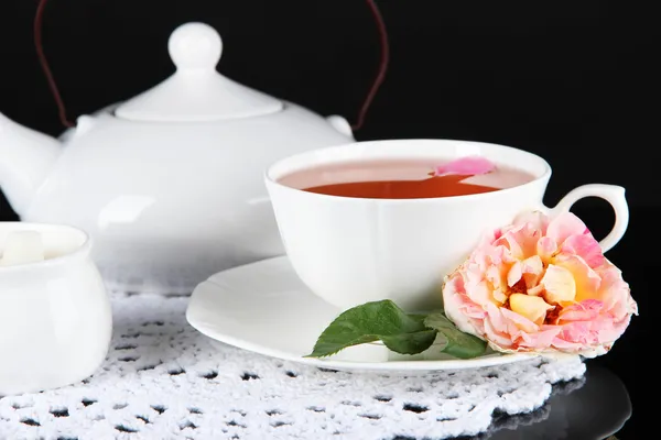 Wasserkocher und Tasse Tee aus Teerose auf Serviette schwarzer Hintergrund — Stockfoto