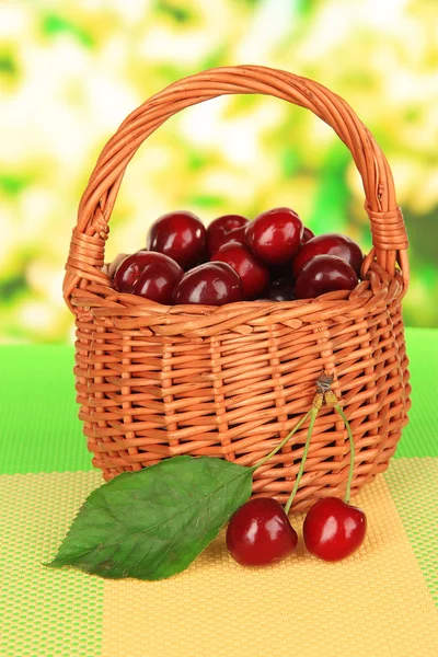 Kirschbeeren im Weidenkorb auf dem Tisch auf hellem Hintergrund — Stockfoto