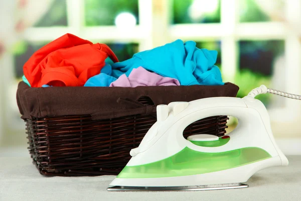 Steam iron and wicker basket with clothes, on bright background — Stock Photo, Image