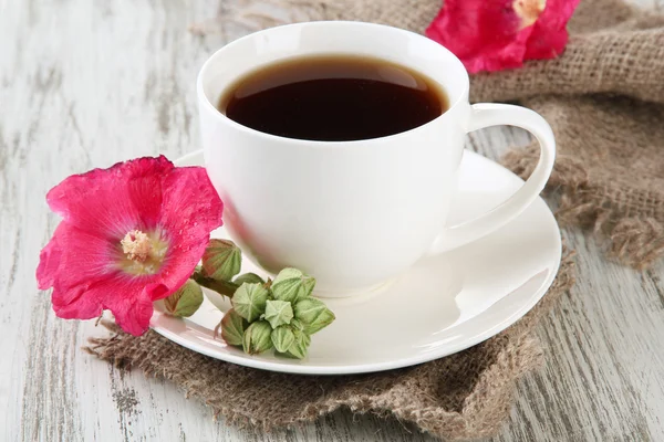 Kopje koffie en roze kaasjeskruid bloemen op houten achtergrond — Stockfoto