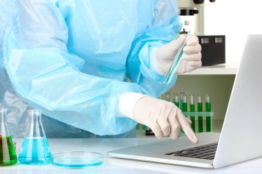 Scientist entering data on laptop computer with test tube close up clipart