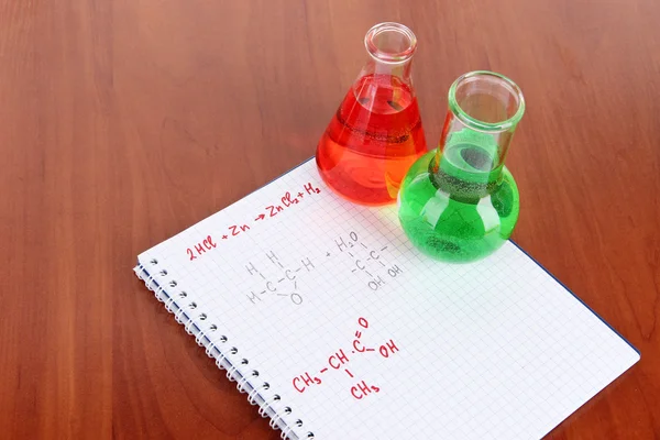 Test tubes with colorful liquids and formulas on table — Stock Photo, Image