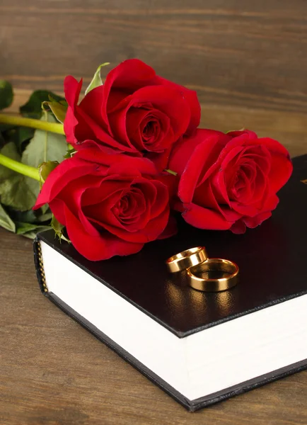 Snubní prsteny na Bibli s růží na dřevěné pozadí — Stock fotografie