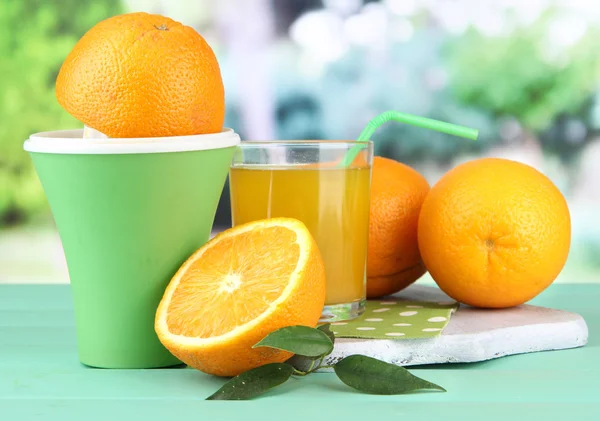 Imprensa de citrinos, copo de suco e laranjas maduras na mesa de madeira verde — Fotografia de Stock