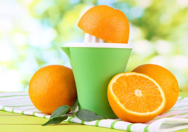 Citrus press and ripe oranges on green wooden table — Stock Photo, Image