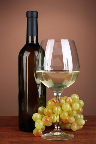 Composition of wine bottle, glass of white wine, grape on color background — Stock Photo, Image