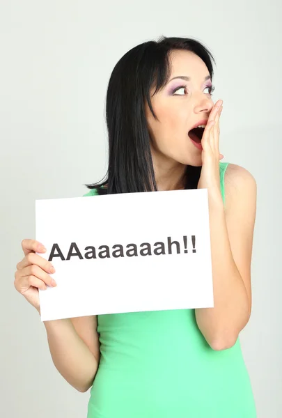 Surprised young woman holds inscription "ah" on grey background — Stock Photo, Image