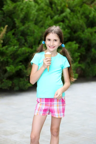 Маленькая девочка катается на коньках есть вкусное мороженое на фоне парка — стоковое фото
