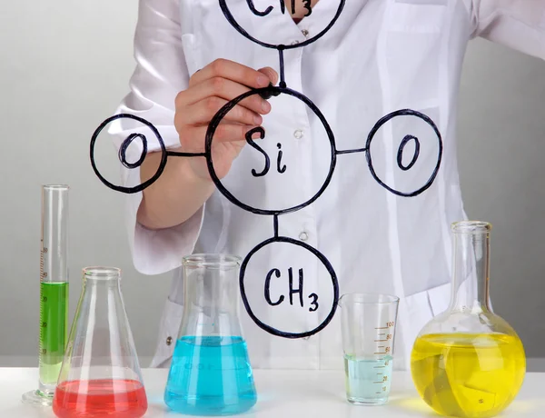 Chemik žena psaní vzorců na sklo na šedém pozadí — Stock fotografie