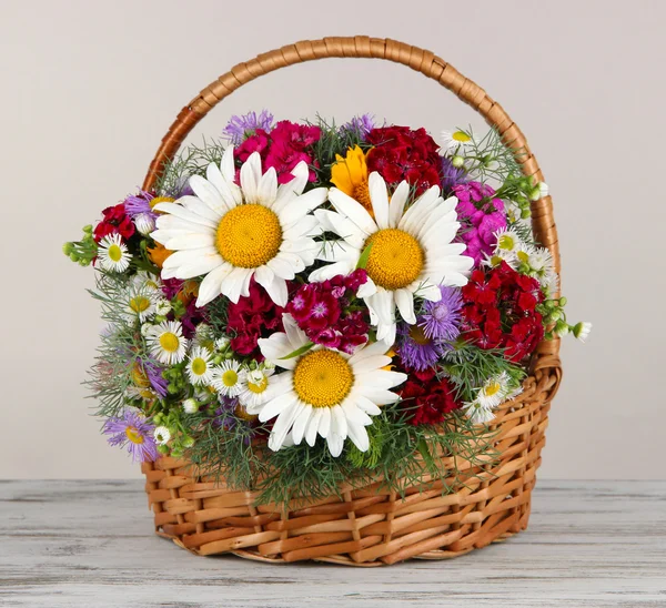 Belles fleurs lumineuses dans le panier en osier sur la table sur fond gris — Photo