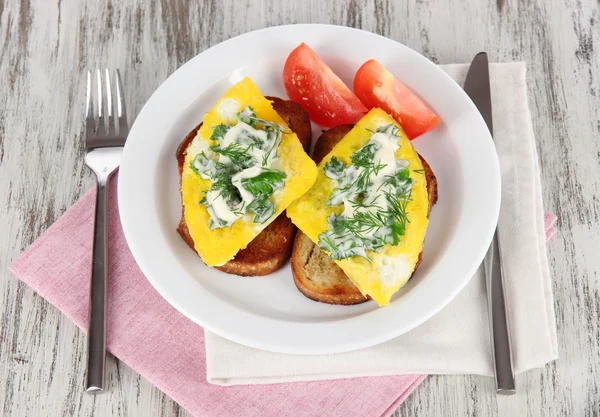 Scrambled eggs and toast on plate on napkin on wooden table — Stock Photo, Image