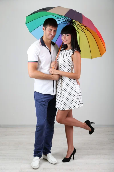 Beautiful loving couple with umbrella on grey background — Stock Photo, Image