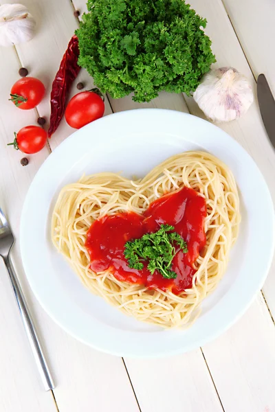 Cooked spaghetti carefully arranged in heart shape and topped with tomato sauce, on wooden background — Stock Photo, Image