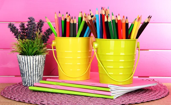 Lápis coloridos em pails com copybooks na mesa sobre fundo rosa — Fotografia de Stock