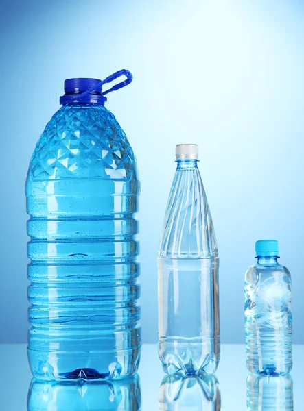 Różne butelki wody na niebieskim tle — Zdjęcie stockowe