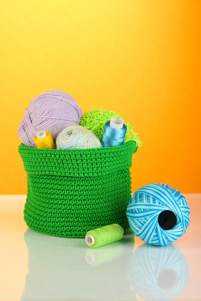 Colorful yarn for knitting in green basket on orange background — Stock Photo, Image