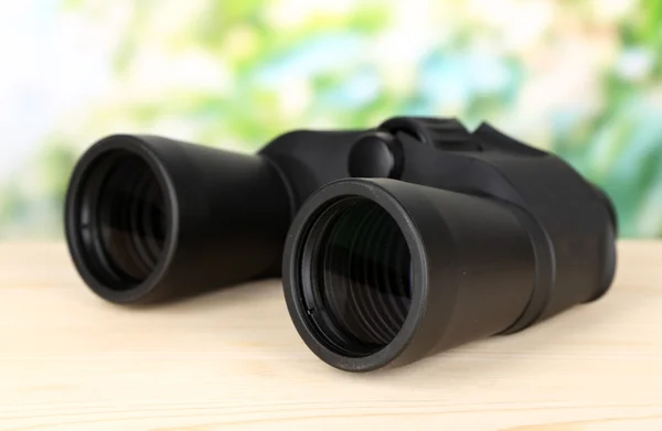 Black modern binoculars on wooden table on green background — Stock Photo, Image